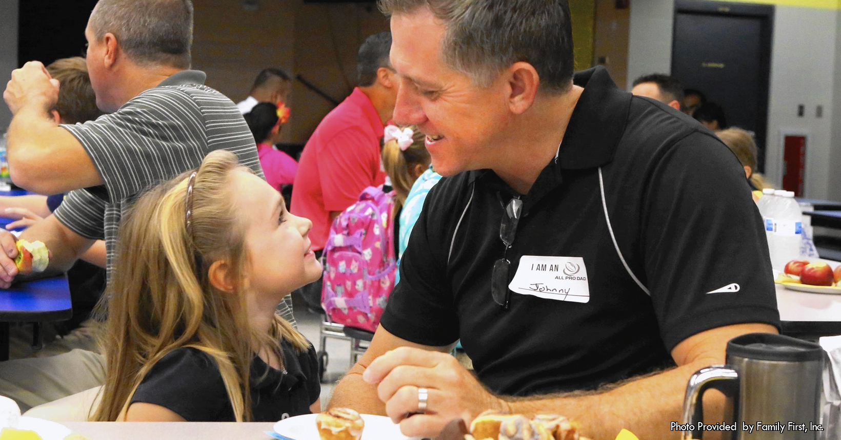 A man and a young enjoy a meal in her elementary school cafeteria.