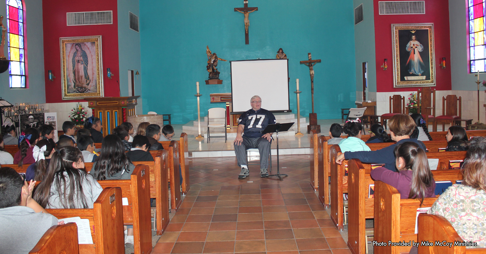 In this photo Mike McCoy is giving a presentation during one of his assembly’s.  This photo was taken for  and given to us by Mike McCoy’s organization, Mike McCoy Ministries.  Standing in the center of the photo is Mike McCoy. Here Mike is giving the kids a faith-based message of hope and encouragement.  With this message he wants to make sure that all the young children will be equipped to the point that no matter what challenge comes against them, they will rise against it. Kids of their age deal with a lot of different things and one of the main things is peer pressure.  In addition to peer pressure, the children maybe struggling with suicidal thoughts, cutting, abuse whether sexual or physical, depression and other serious problems. However after the conversation between them he will instill in them a greater amount of self-confidence.