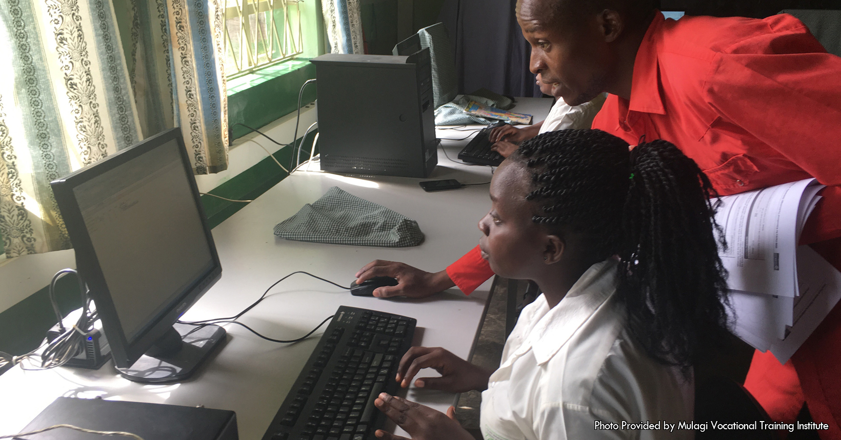 Interior shot of the classroom where an instructor teaches a woman how to use a computer