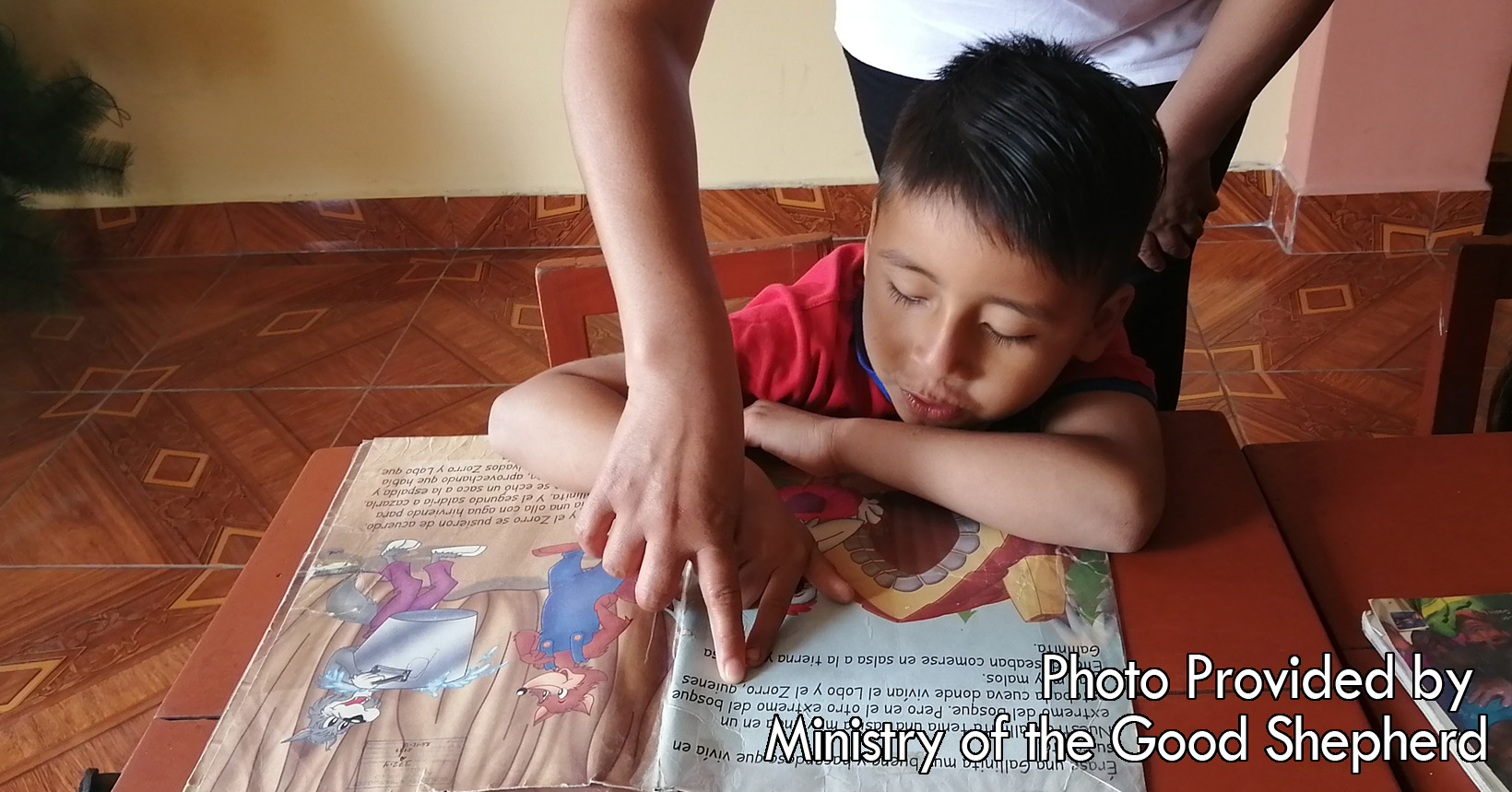 A sister is helping this young boy learn how to read. She is guiding him from one sentence to another to make sure that he is pronouncing his words correctly.