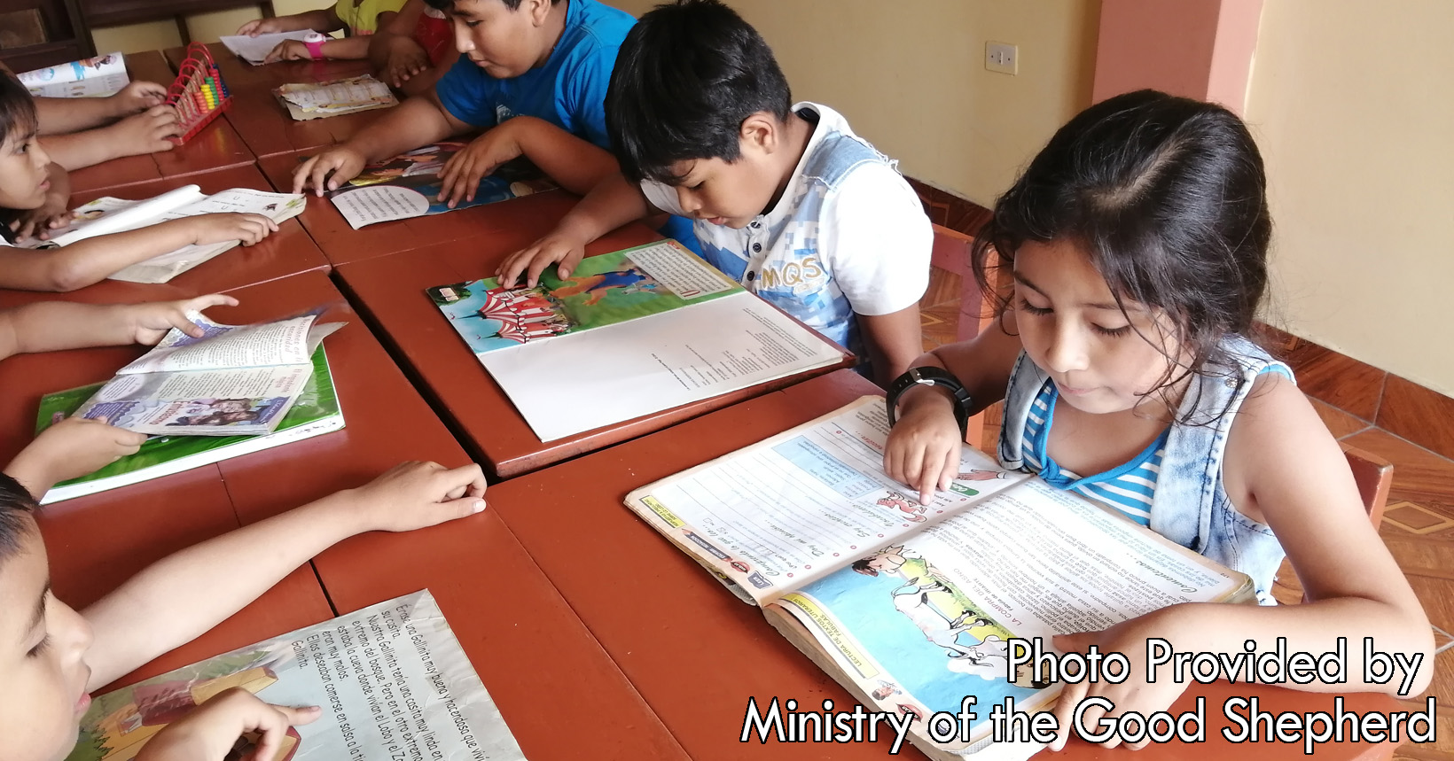 The young children are gathered around each other in the pursuit of learning. Each one is silently reading their picture books expanding their vocabulary.