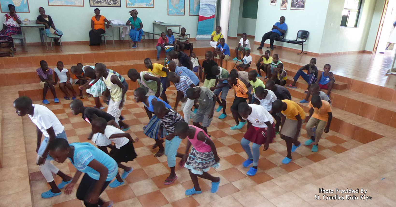 A large group of children dance in the auditorium.