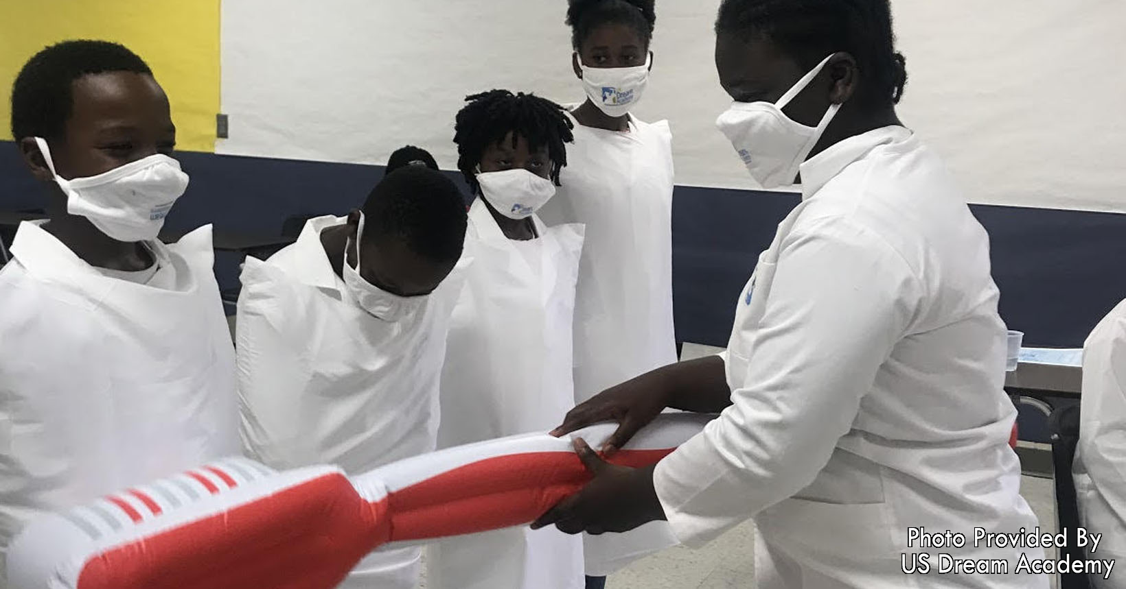 Four children enact teeth while a fifth uses an inflatable toothbrush to demonstrate correct brushing techniques.